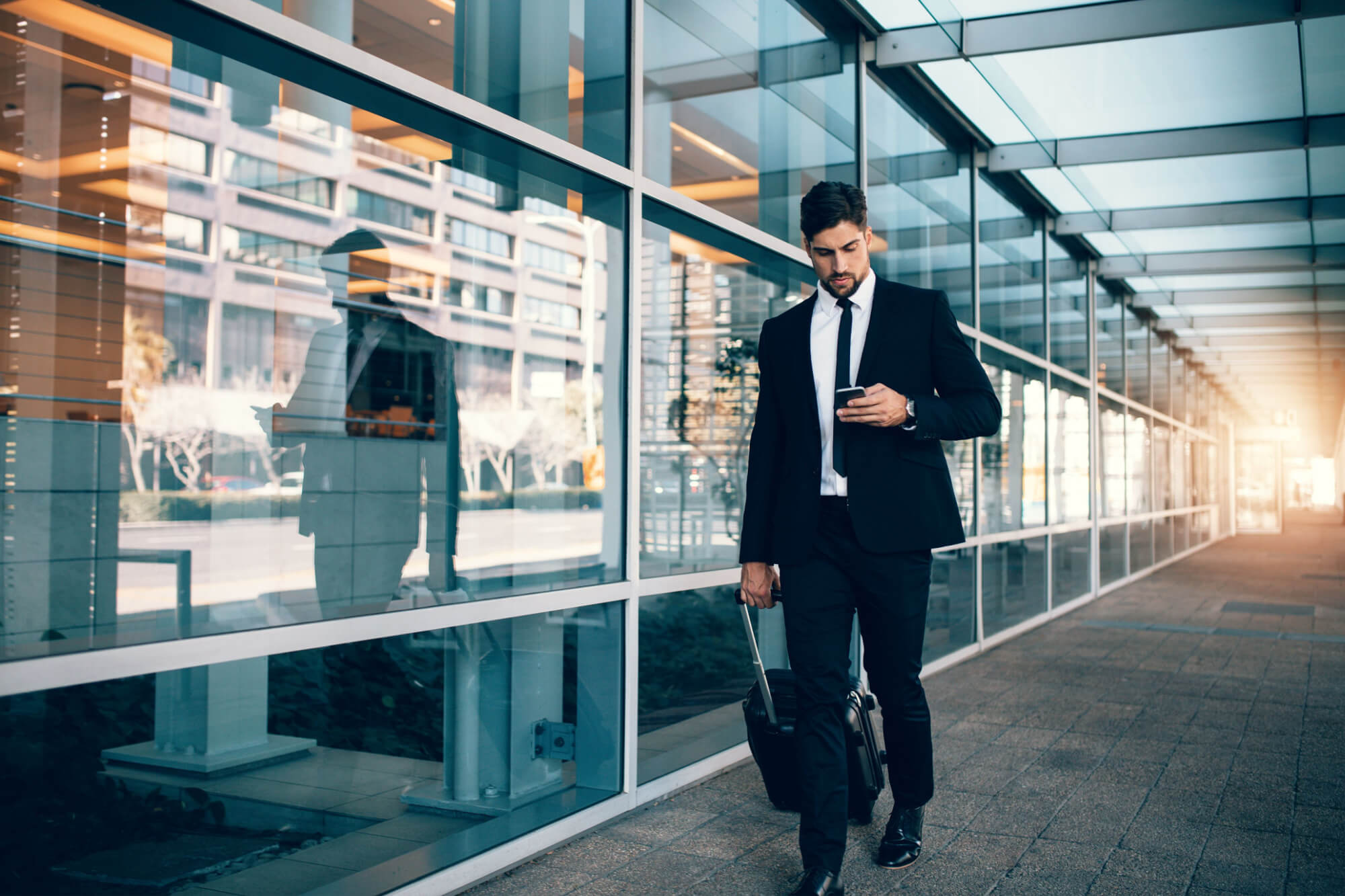 Businessman walking with luggage and using mobile phone at airport