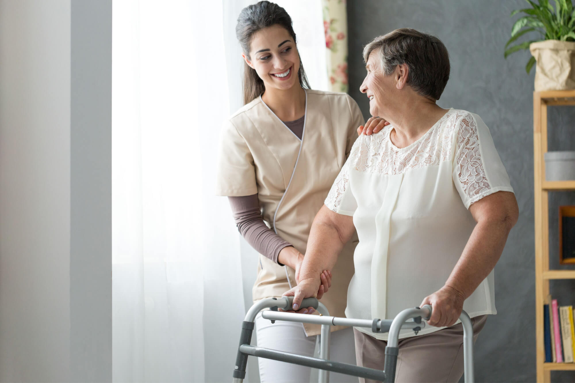 Smiling beautiful caregiver and disabled old lady with walker